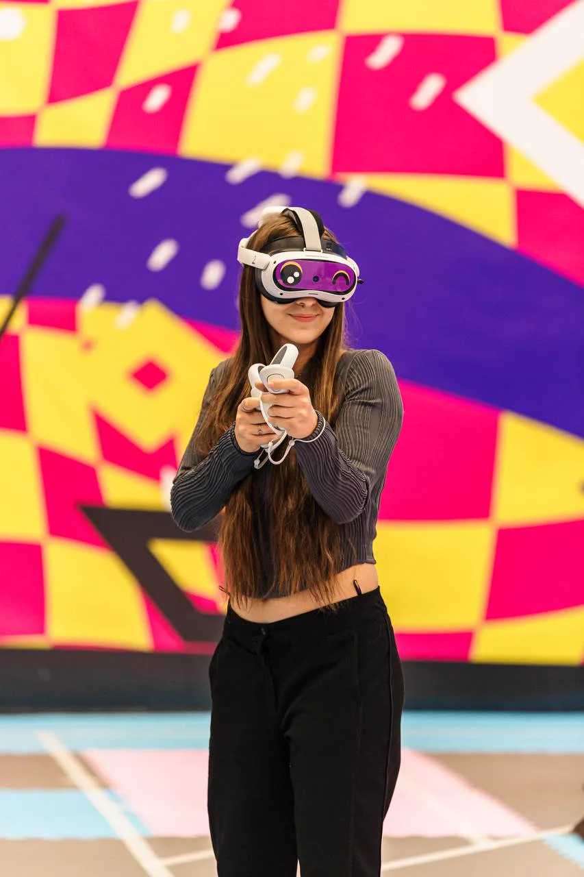 Девушка в VR-шлеме с контроллерами в руках на игровой арене
